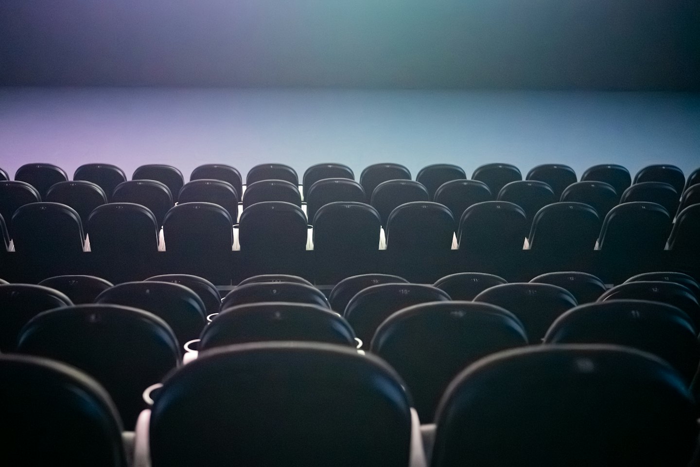 Posti vuoti in un teatro di fronte a una luce sfumata viola, blu e verde.